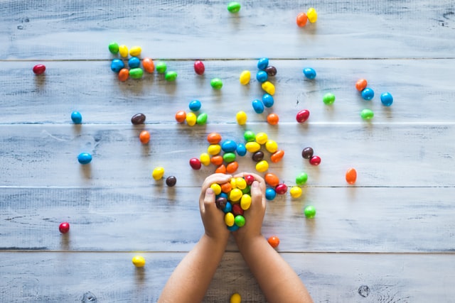 A child's hands arranging colorful candy on a wooden background.