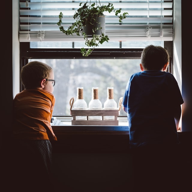 Two boys looking over a window. 