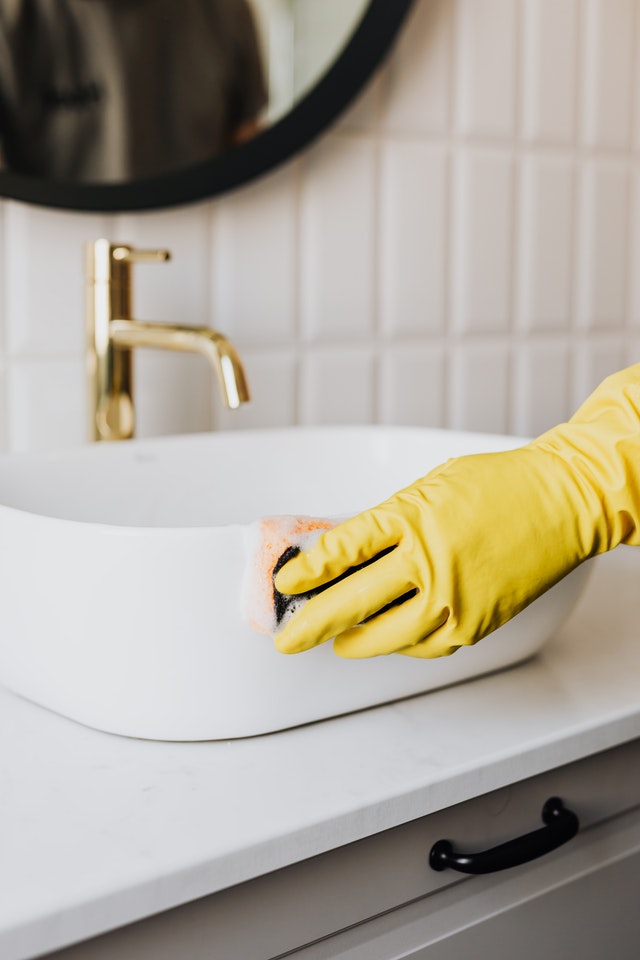 A pair of hands in yellow cleaning gloves wiping a bathroom sink.