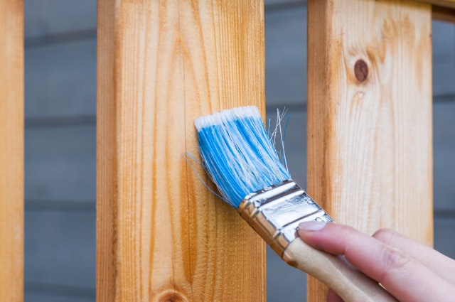 A hand painting a wooden plank with a paint brush.