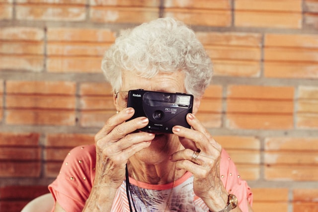 An elderly woman clicking a photo with an analog camera