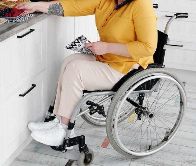 A woman sitting in a wheel chair reaching out to a kitchen counter