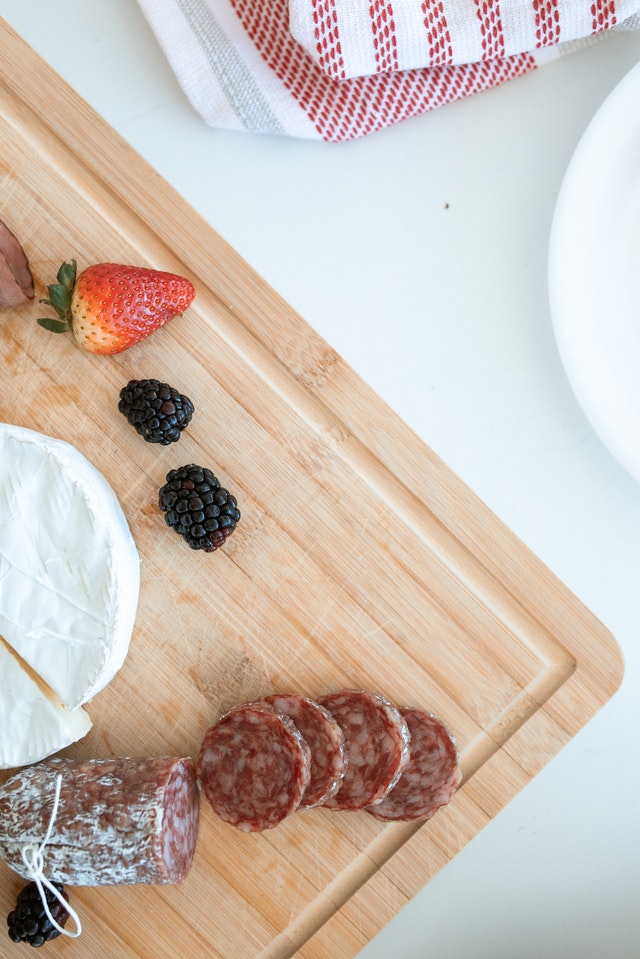 meats, cheese and strawberries arranged on a wooden board