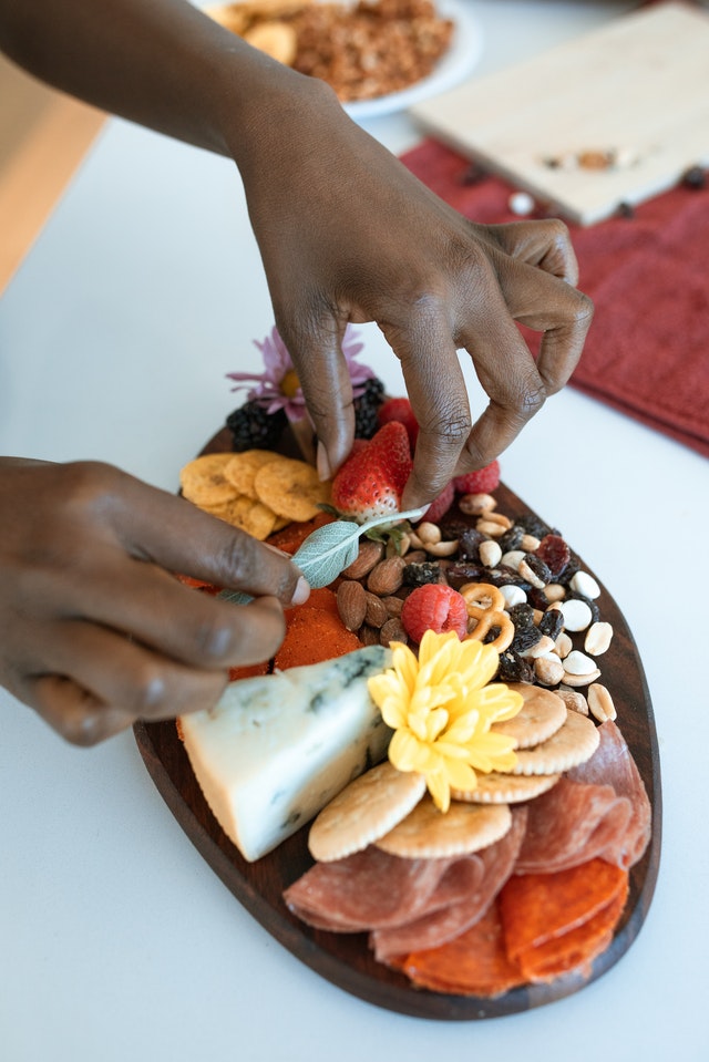 A hand adding basil leaf to a charcuterie and cheese board