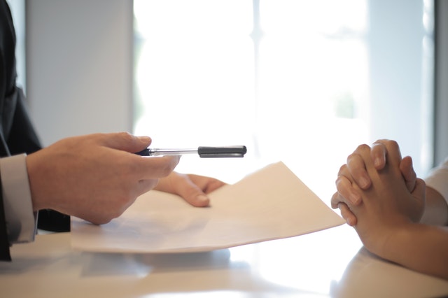 Two people sitting across from each other with one hand holding a pen and a paper