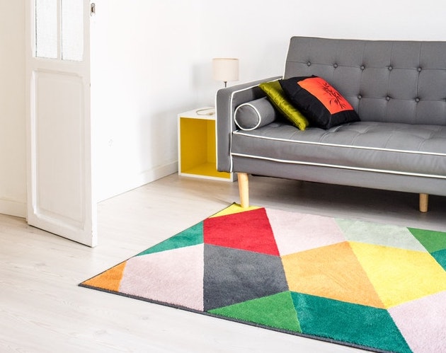 A bright rug laid out under a grey couch
