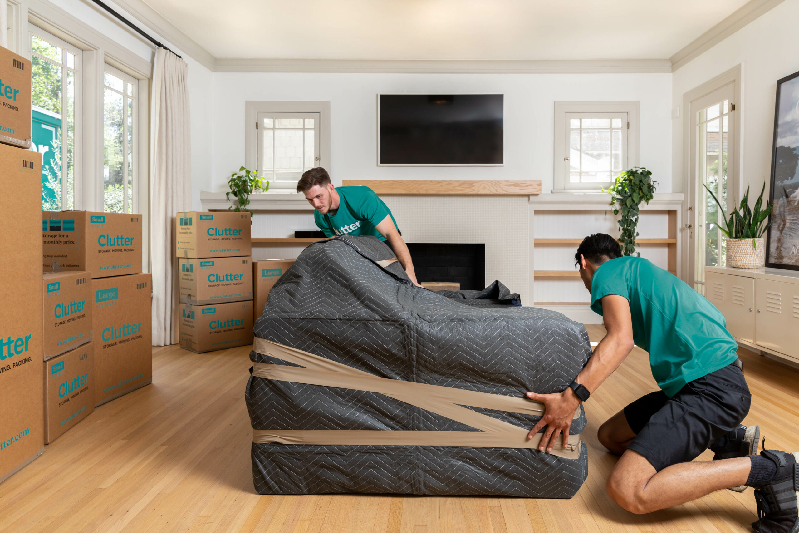 Two members of the Clutter moving team carefully wrapping a piece of furniture in a room surrounded by packed Clutter moving boxes.