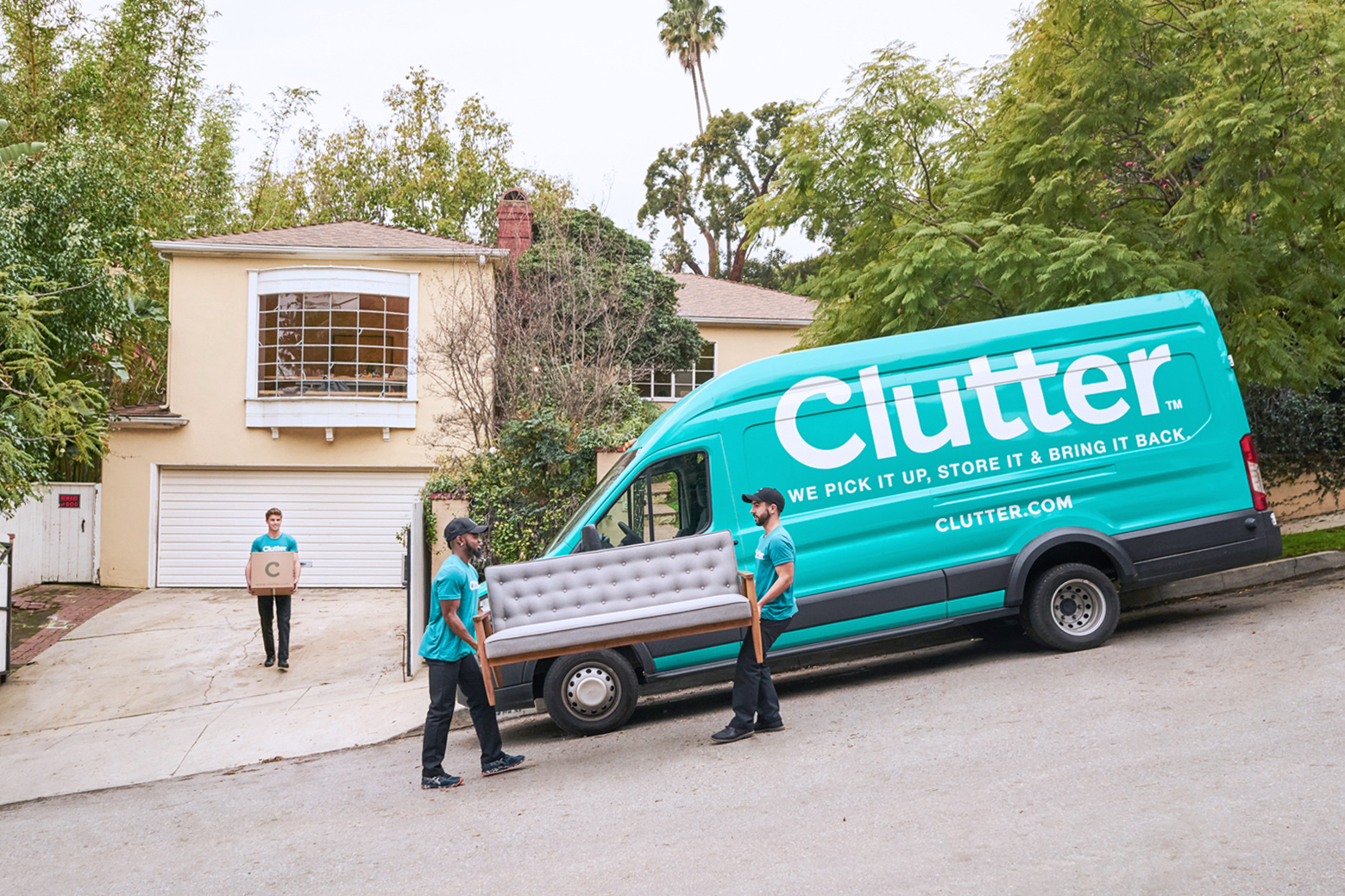Two members of the Clutter moving team moving a couch into a Clutter van, followed by another team member carrying a box. Moving large items would contribute to how much you tip.