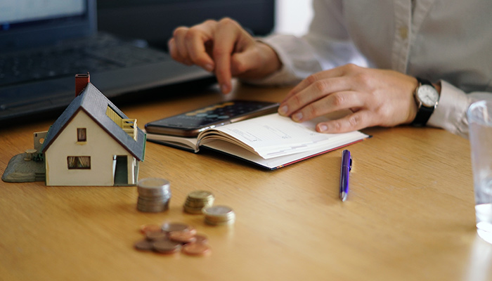 man calculating expenses on his phone with a notebook and a miniature home on a table 